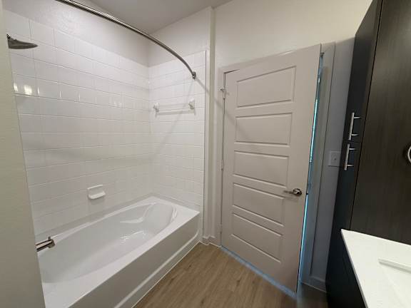 A white tiled bathroom with a white bathtub and a white door.