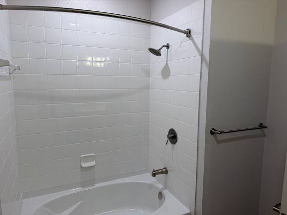 A white tiled bathroom with a white tub and a shower head.