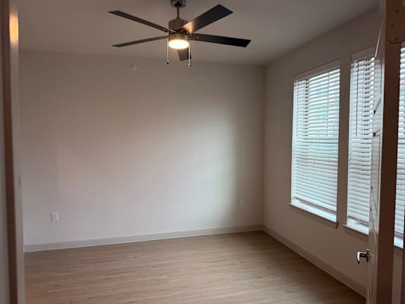 A room with a ceiling fan and a window with blinds.