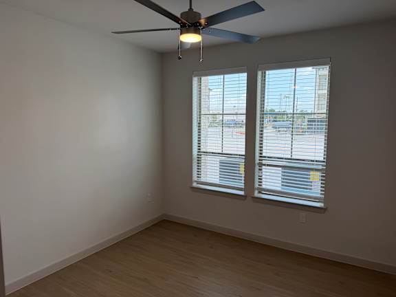 A room with a ceiling fan and two windows with blinds.