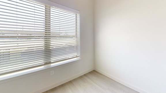 A room with a window covered by white blinds.