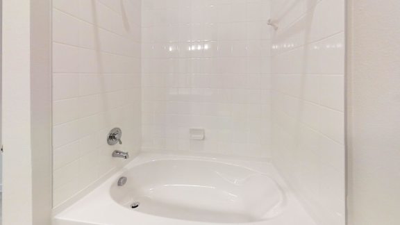 A white bathtub in a bathroom with a white tile wall.
