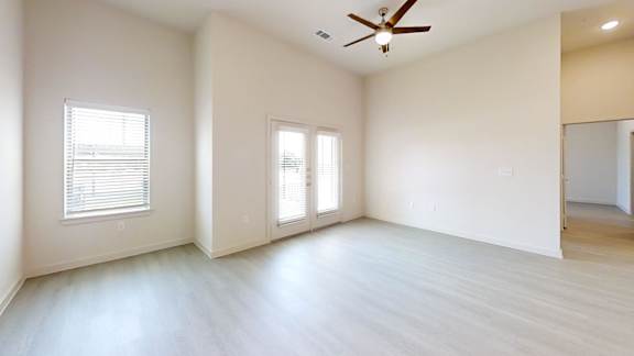 A spacious room with a ceiling fan and two windows.