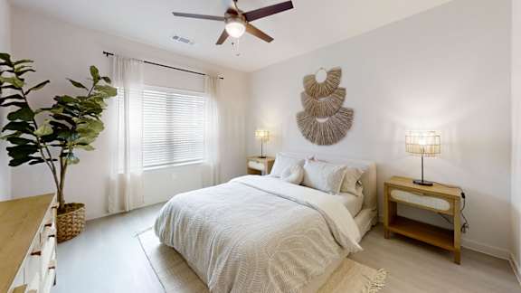 A bedroom with a bed, a ceiling fan, and a plant.