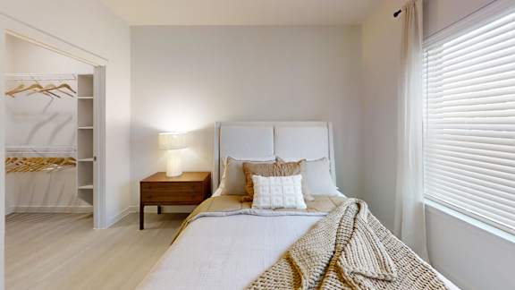 A bedroom with a bed, nightstand, and window with blinds.