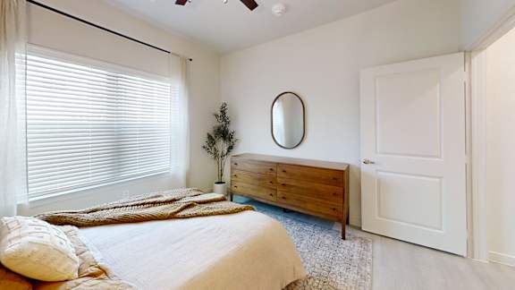 A bedroom with a bed, dresser, and window with blinds.