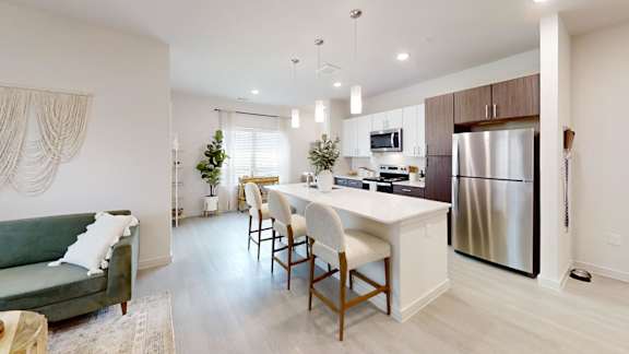 A modern kitchen with a green couch and wooden chairs.