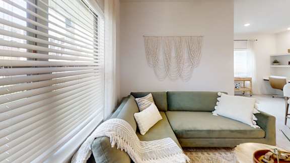 A living room with a green couch and a white wall hanging.