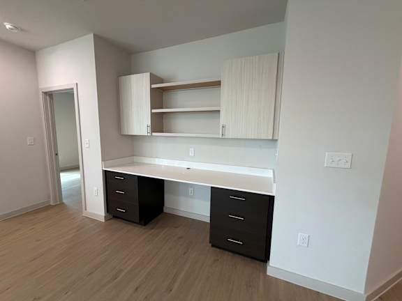 A white desk with black drawers is in a room with white walls and wood flooring.
