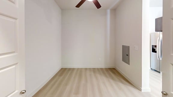 A white room with a ceiling fan and a refrigerator.