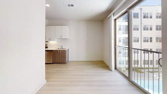 A spacious room with a kitchen area and a balcony with a railing.