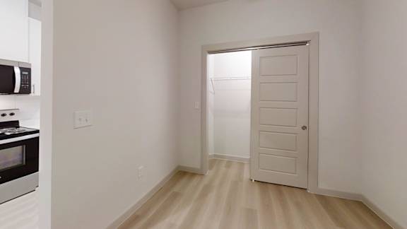 A white door is open in a room with wooden flooring. at Bridge at Saffron Apartments, Texas
