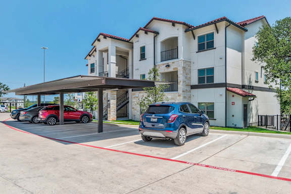 A blue car is parked in a parking lot in front of a building. at Bridge at Delco Flats Apartments, Texas