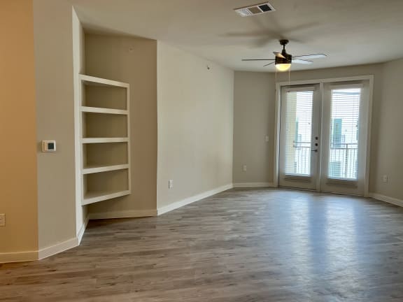 an empty living room with a bookshelf and a ceiling fan