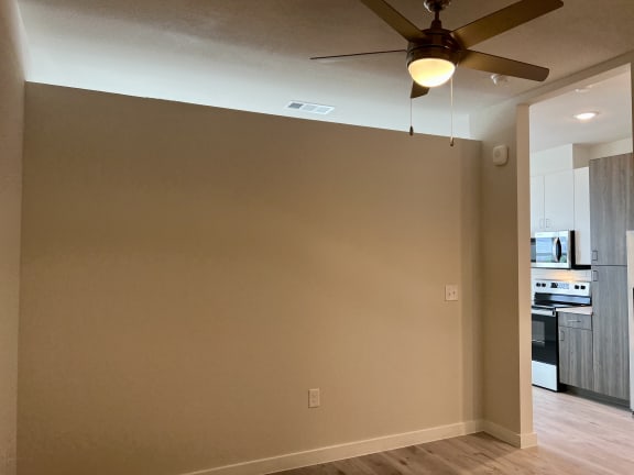 a living room with a ceiling fan and a kitchen in the background