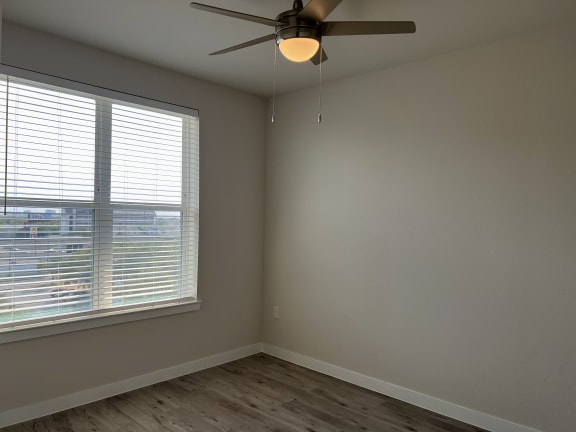 Empty bedroom with large window and laminate flooring at Bridge at Windsor Park Apartments, Texas