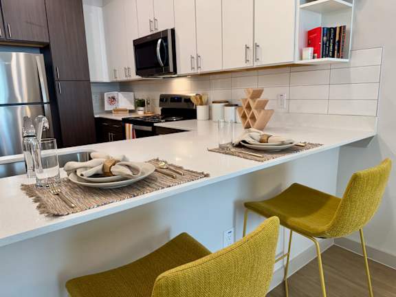 A modern kitchen with a white countertop and yellow chairs.