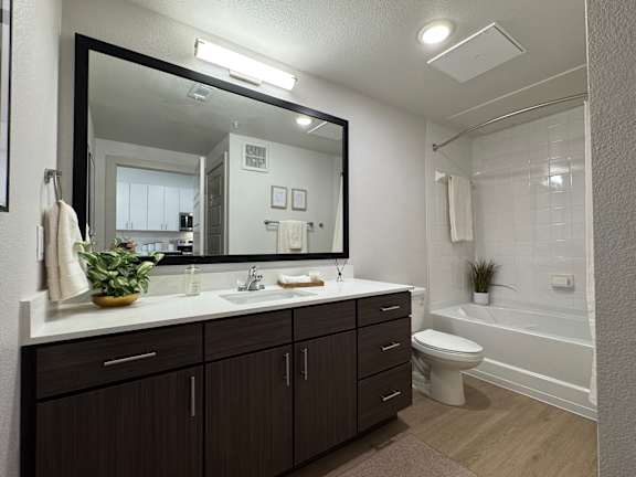 A bathroom with a large mirror, a white sink, and a white toilet.