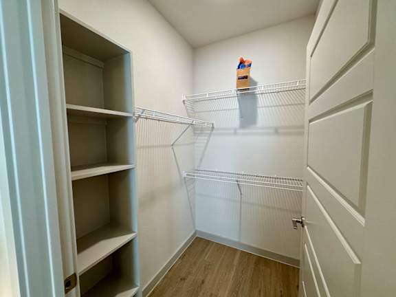 A small, empty walk-in closet with a wooden floor and white walls.