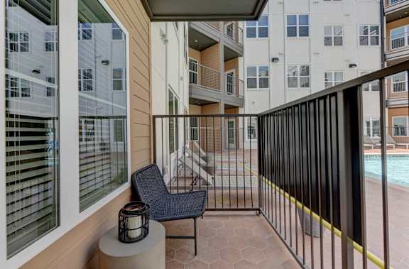 A balcony with a black chair and a lantern on a table. at Park South Apartments, Texas