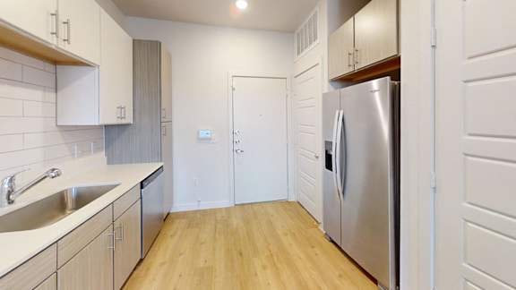 A kitchen with a refrigerator, sink, and wooden floors.