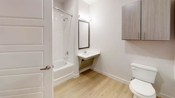 A white toilet sits in a small bathroom with a white door and a white cabinet. at Park South Apartments, Austin, 78748