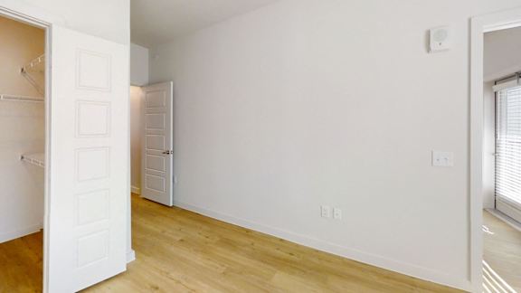 A white door is open to a room with wooden floors and white walls.