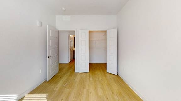 A room with white walls and wooden flooring with a doorway leading to another room.