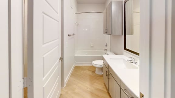 A white bathroom with a toilet, sink, and mirror. at Park South Apartments, Austin, TX, 78748