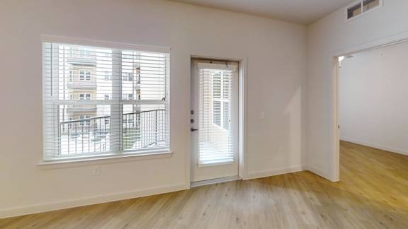 A room with a wooden floor and a window with blinds. at Park South Apartments, Austin, TX