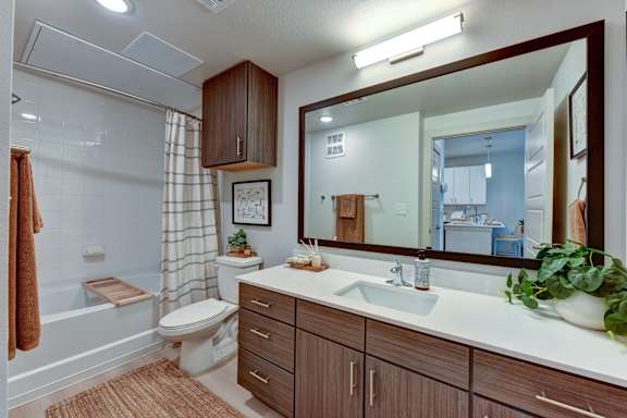 Modern bathroom with wood vanity and large mirror at Bridge at Saffron Apartments, Texas