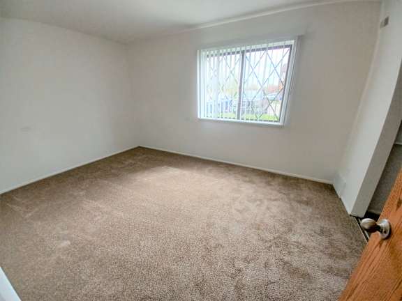 Empty carpeted bedroom with window and security bars at Charter Oaks Apartments, Davison, Michigan