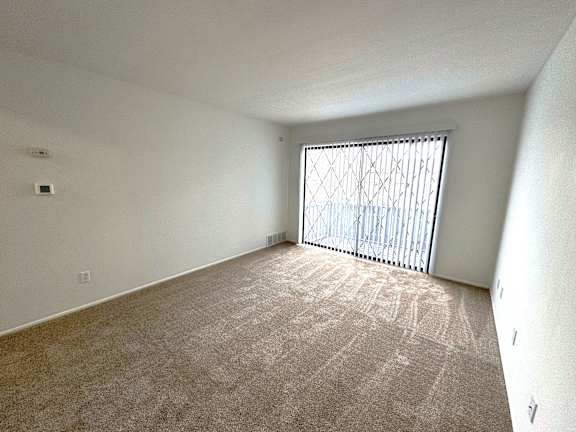 Empty carpeted room with vertical window blinds at Charter Oaks Apartments, Davison, MI, 48423