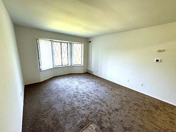 Empty carpeted living room with window blinds at Charter Oaks Apartments, Davison, MI, 48423