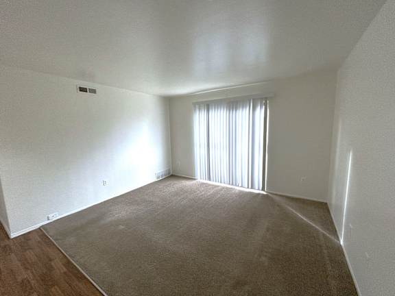 A living room with a carpeted floor and a window with blinds.