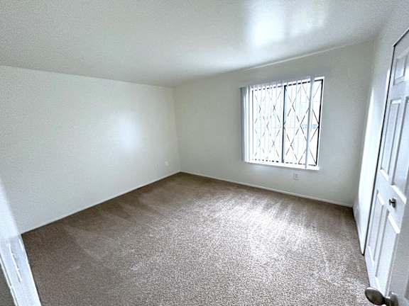 A bedroom with a carpeted floor and a window with bars.