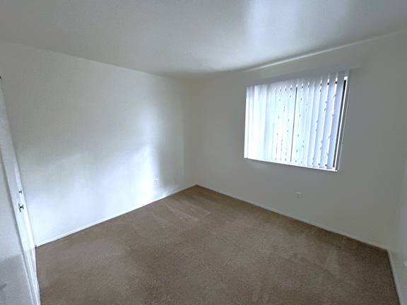 A bedroom with a window covered by white blinds.