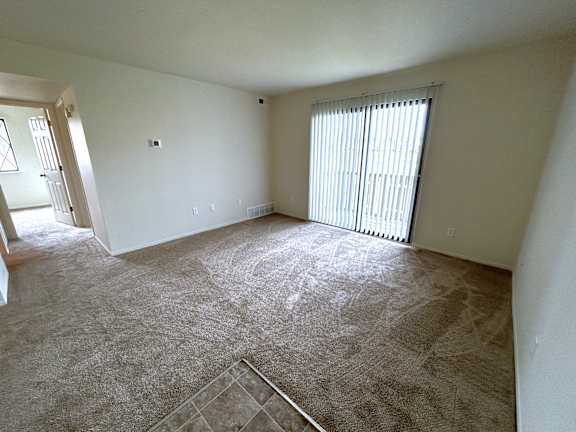 A living room with a carpeted floor and a window with blinds.