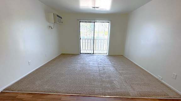 A spacious living room with a carpeted floor and a sliding glass door.