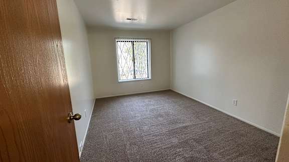 A bedroom with a carpeted floor and a window with bars.