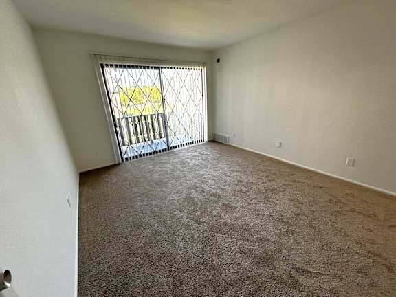Empty carpeted room with sliding door and balcony access at Charter Oaks Apartments, Michigan, 48423