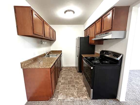Galley kitchen with black appliances and brown cabinetry at Charter Oaks Apartments, Michigan