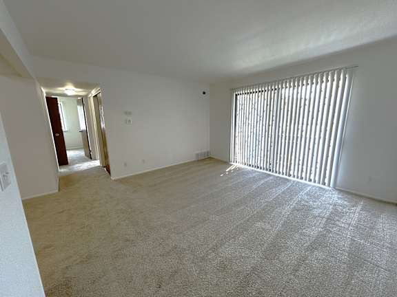 A living room with a carpeted floor and a window with blinds.