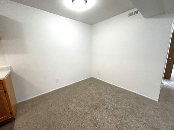 A dining room with a carpeted floor and a wooden cabinet on the left side.