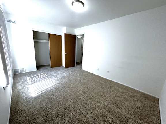 A bedroom with carpeted floor and two brown doors.