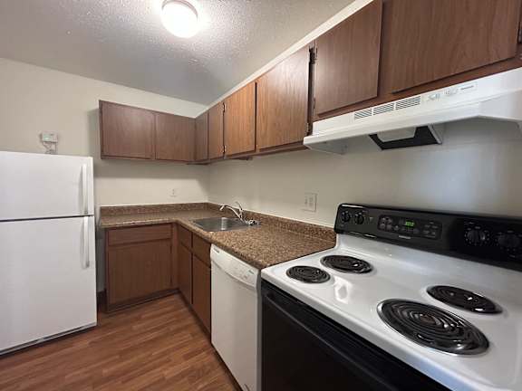 A kitchen with a white fridge, black stove, and brown cabinets.