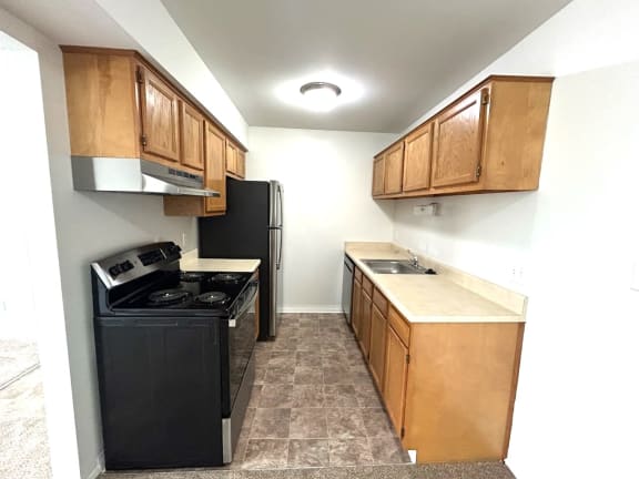Galley kitchen with stainless refrigerator and black stove at Charter Oaks Apartments, Davison