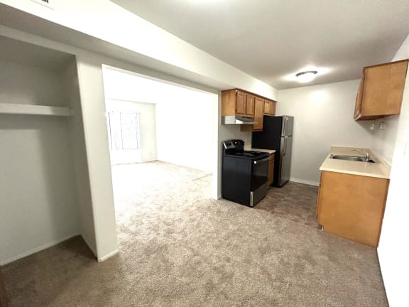 Open layout kitchen with black appliances and beige carpet at Charter Oaks Apartments, Davison, Michigan