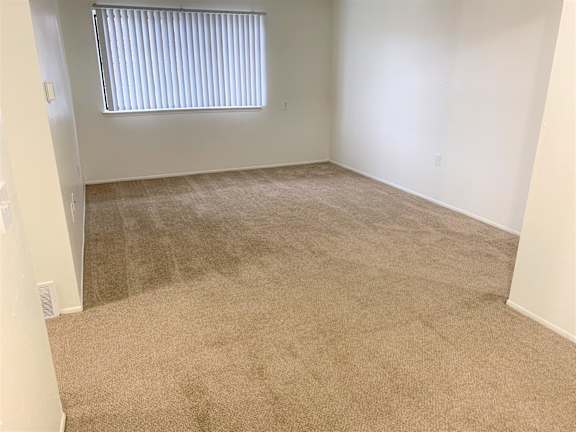 A living room with a carpeted floor and a window with blinds.