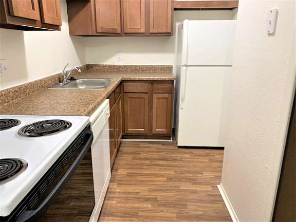 A kitchen with a white stove top oven, white fridge, brown cabinets and a brown counter top.